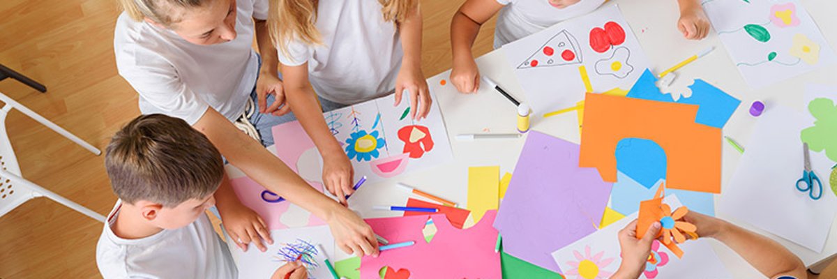 auf dem Foto sind Kinder an einem Tisch von oben zusehen auf dem Tisch liegt ganz viel Buntpapier