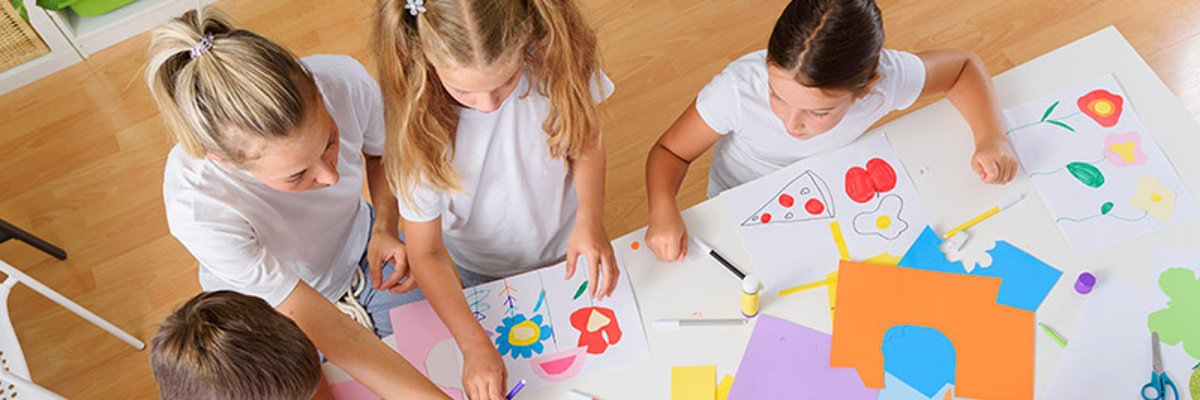 auf dem Foto sind Kinder an einem Tisch von oben zusehen auf dem Tisch liegt ganz viel Buntpapier
