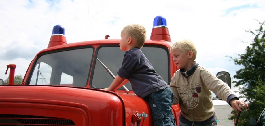 Auf dem Bild sind zwei Kinder auf einem Feuerwehrauto zu sehen