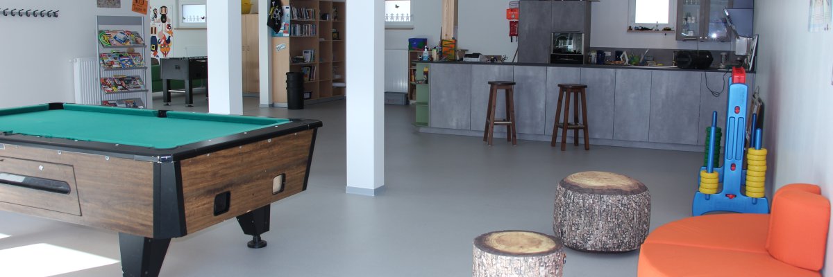 auf dem Foto ist der Jugendraum von innen zu sehen ein Billardtisch und eine Theke mit Barhockern davor