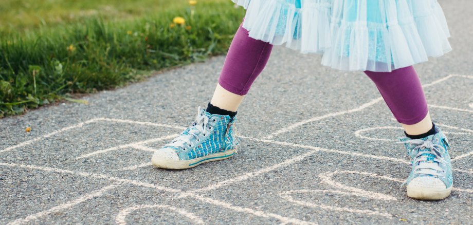 Auf dem Bild sind aufgemalte Hüpfekästchen zu sehen und Kinderschuhe