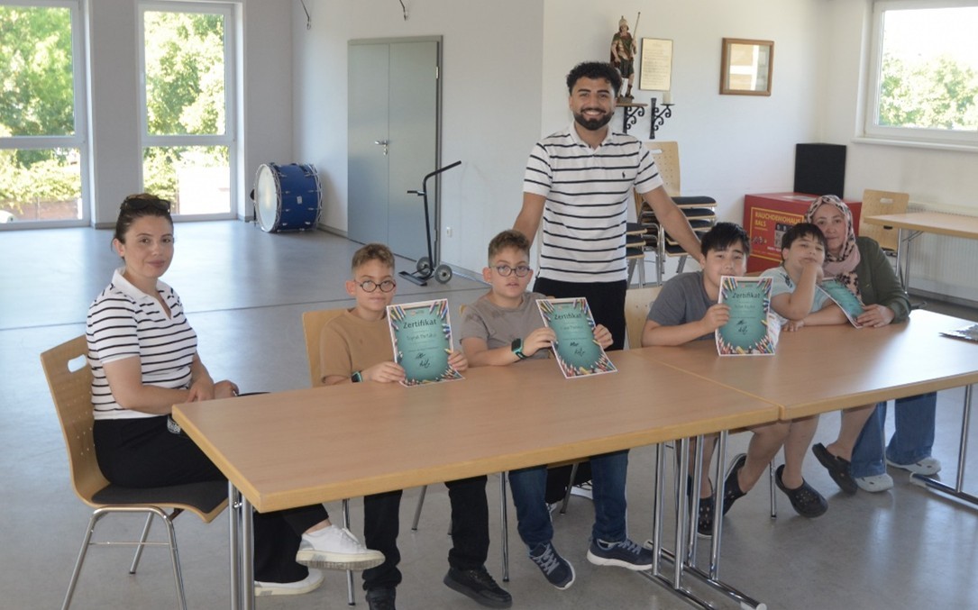 Kinder und eine Frau an einen Tisch sitzend ein Mann stehend