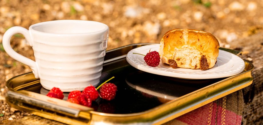 Auf dem Bild ist eine Tasse Kaffee und Gebäck mit ein paar Himbeeren zu sehen