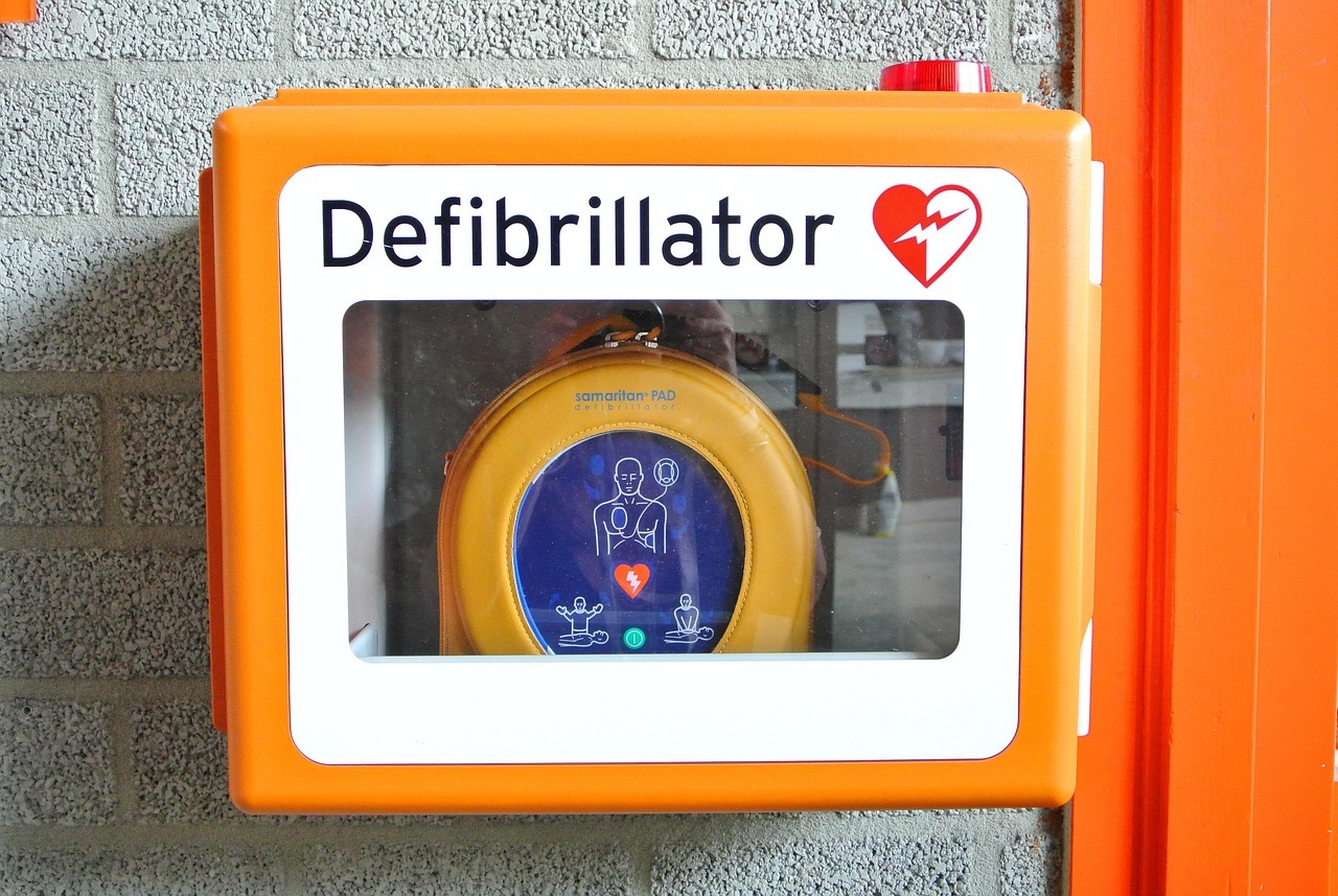 Auf dem Bild ist ein Defibrillator, der an einer gemauerten Wand hängt, abgebildet.
