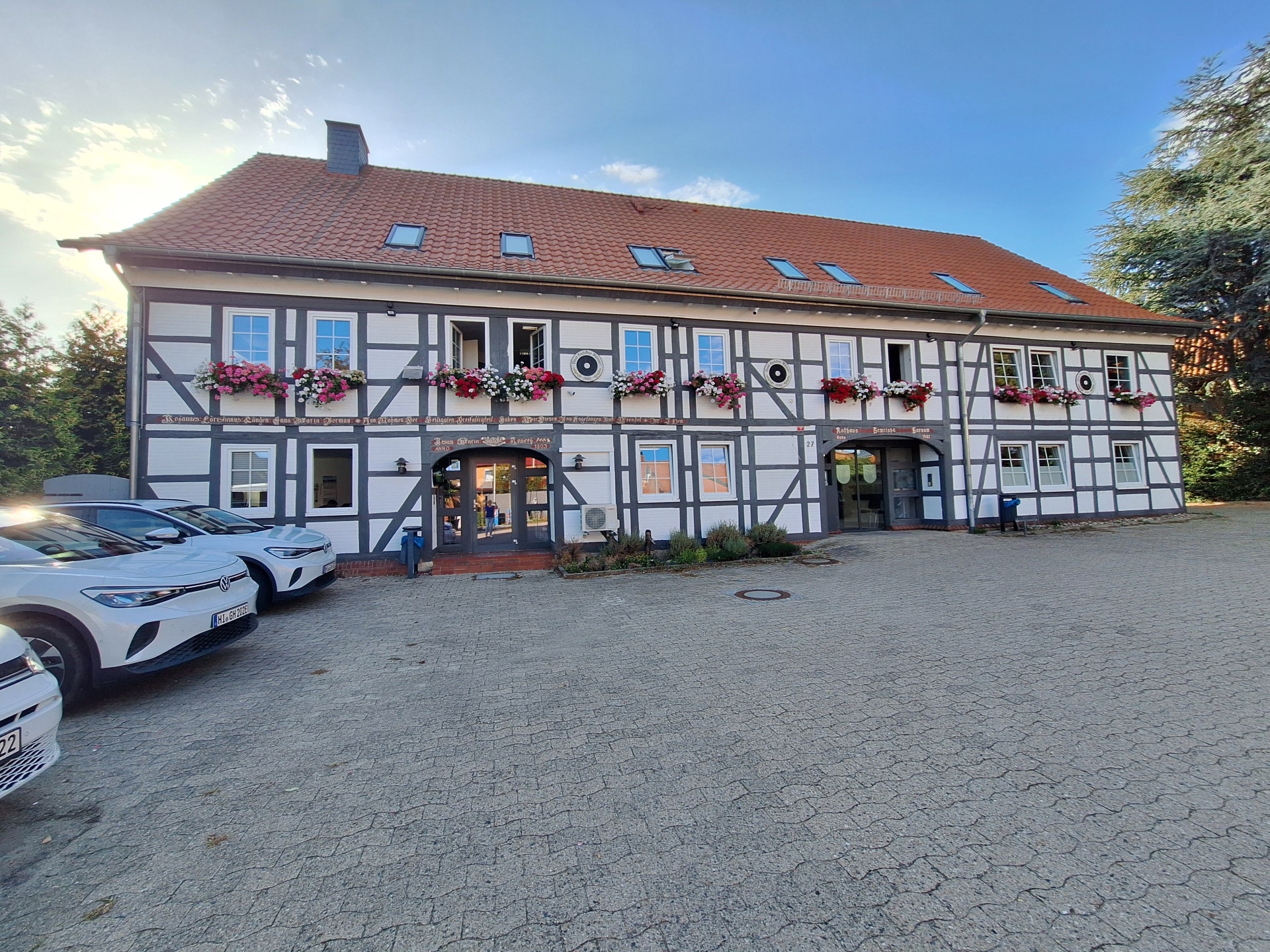 auf dem Foto ist das Harsumer Rathaus zu sehen. Die Geranien blühen in Blumenkästen an den Fenstern in der 1. Etage. Der Himmel ist blau