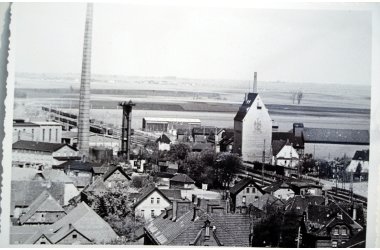 auf dem Schwarzweiß Foto ist der hohe Schornstein der Zuckerfabrik und das Silo der HG zu sehen. Es handelt sich um eine Luftaufnahme