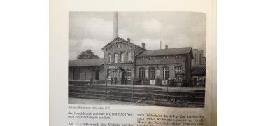 Das schwarzweiß Foto zeigt das damalige Bahnhofsgebäude mit Bahnsteig und Schienen im Vordergrund