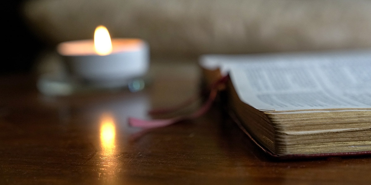 Open bible with burning candle on the table