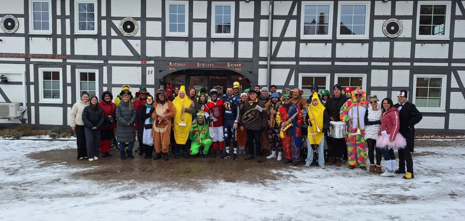 auf dem Foto sind der Musikzug der freiwilligen Feuerwehr und Rathausmitarbeiter bunt verkleidet vor dem verschneiten Rathaus zu sehen